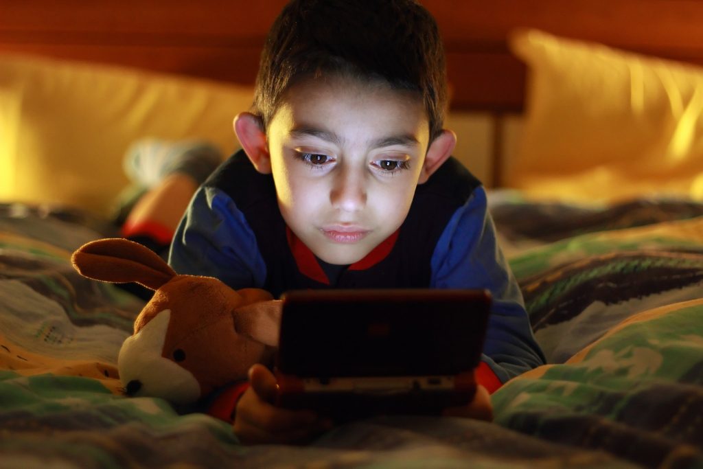 kid in bed wih videogame console on night